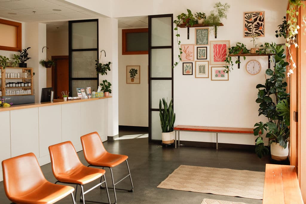Clinic lobby with reception desk, botanical gallery wall, and abundant greenery