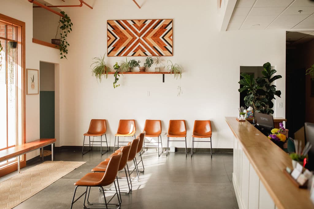 Bright clinic waiting area with leather seating, geometric wood art, plants, and a reception desk